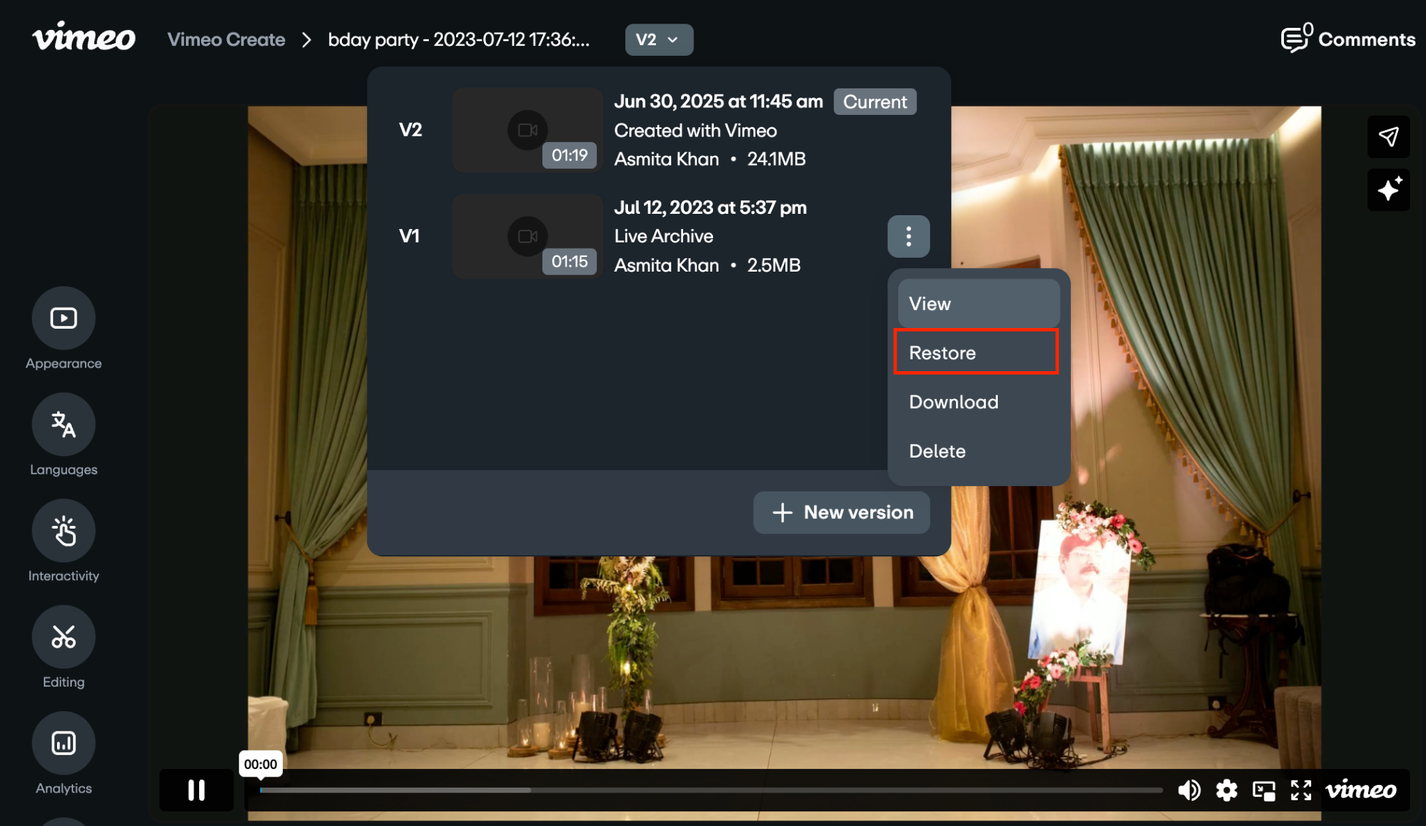 Tela do reprodutor de vídeo mostrando o pop-up do histórico de versões. O menu de três pontos ao lado de V1 está aberto, mostrando as opções "Ver", "restaurada", "Baixar" e "Excluir", com "restaurada" em destaque.
